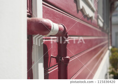red wall with pipe, illuminated by sun, displaying modern urban design with vibrant colors red wall with pipe, illuminated by sun, displaying modern urban design with vibrant colors 115836420