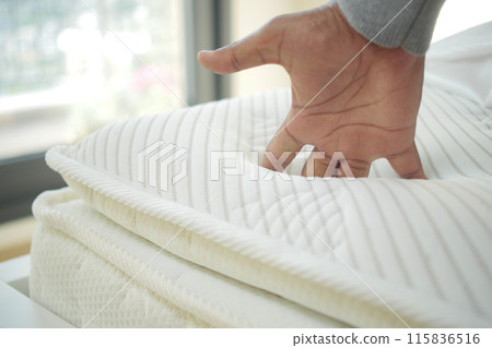Hand touching and pressing orthopedic mattress on bed. 115836516