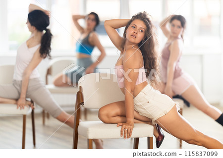 Girl sitting on knees on chair performs lap dance. Female students repeat erotic movements 115837099