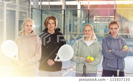 Four paddle tennis players standing on court holding rackets and balls after match 115837150