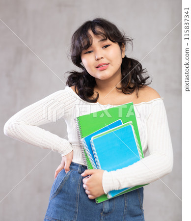 Smiling young girl with notebooks posing in studio Smiling young girl with notebooks posing in studio 115837341