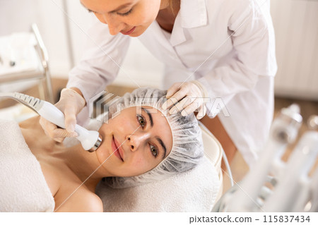 Young female cosmetologist doing ultrasound procedure to young woman Young female cosmetologist doing ultrasound procedure to young woman 115837434