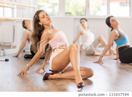 Girls perform dance in heels, squat down, actively repeat movements of instructor. 115837594
