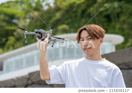 Japanese man enjoying drone photography outdoors on a sunny day | Drone image Japanese man enjoying drone photography outdoors on a sunny day | Drone image 115838117