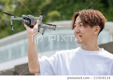 Japanese man enjoying drone photography outdoors on a sunny day | Drone image Japanese man enjoying drone photography outdoors on a sunny day | Drone image 115838118