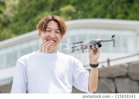 Japanese man enjoying drone photography outdoors on a sunny day | Drone image Japanese man enjoying drone photography outdoors on a sunny day | Drone image 115838141