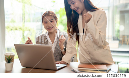 Two cheerful Asian businesswomen are celebrating their business project success together. 115839359