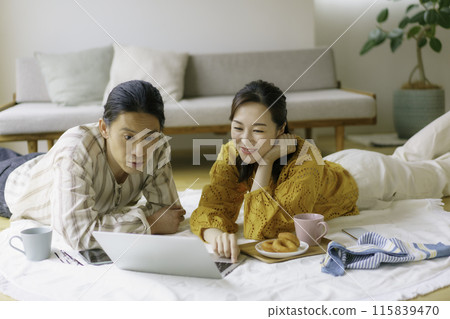A young couple lying on the living room floor looking at a typing computer A young couple lying on the living room floor looking at a typing computer 115839470