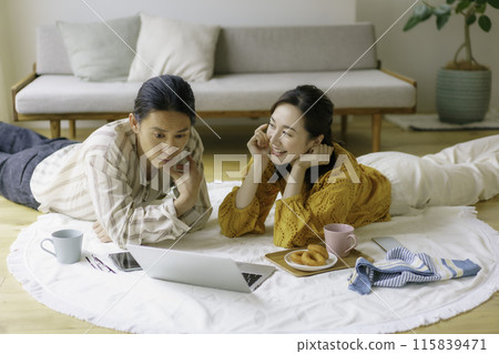 A young couple lying on the living room floor looking at a typing computer 115839471