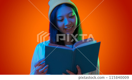 Enjoying reading. Woman book. Cheerful focused female holding textbook exciting education rest happy pastimes green blue neon light isolated on red gradient empty space background. Enjoying reading. Woman book. Cheerful focused female holding textbook exciting education rest happy pastimes green blue neon light isolated on red gradient empty space background. 115840009