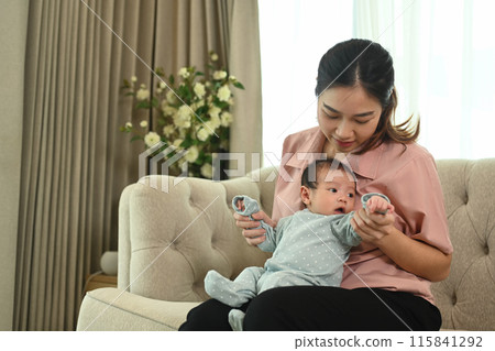 Happy smiling mother with cute infant little baby boy sitting on couch at home. Motherhood and child care concept 115841292