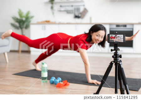 Woman in plank pose recording fitness video at home 115841295