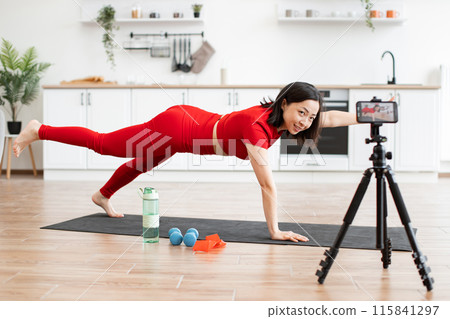 Woman in plank pose filming yoga tutorial at home kitchen Woman in plank pose filming yoga tutorial at home kitchen 115841297