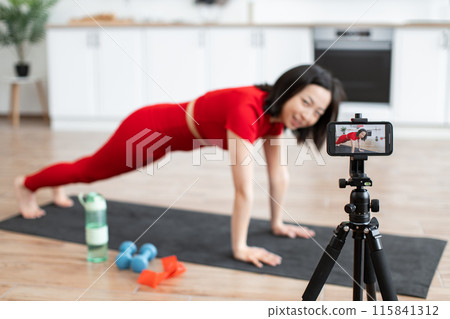 Woman recording workout video at home in red sportswear 115841312