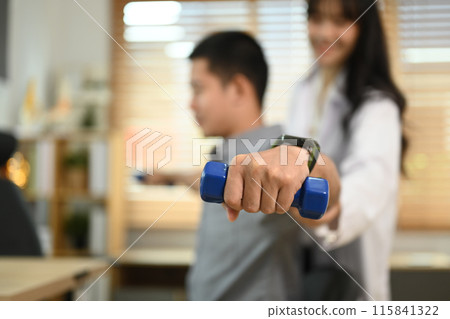Focused on hand of patient lifting weights under therapist guidance. Rehabilitation and health care concept Focused on hand of patient lifting weights under therapist guidance. Rehabilitation and health care concept 115841322