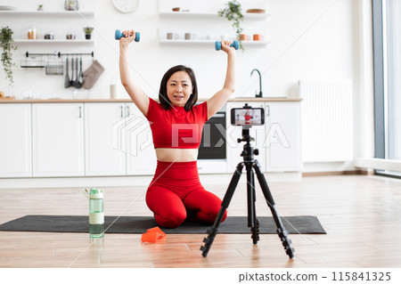 Woman recording workout session at home with dumbbells and tripod 115841325