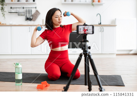 Woman exercising with dumbbells recording online workout at home 115841331