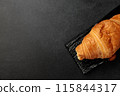 Crispy hot croissant on a black rectangular wooden board on a gray background 115844317