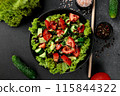 Vegetable salad of tomatoes, cucumbers, onions, lettuce dressed with aromatic dressing in a black plate on a gray background 115844322