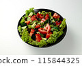 Vegetable salad of tomatoes, cucumbers, onions, lettuce dressed with aromatic dressing in a black plate on a white  background 115844325