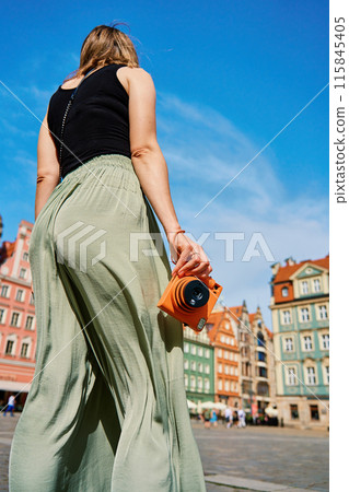 Female tourist captures memories during travel with vintage instant camera 115845405