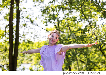 A Cheerful Woman is standing in Nature with her Arms Outstretched on a Sunny Day A Cheerful Woman is standing in Nature with her Arms Outstretched on a Sunny Day 115845913