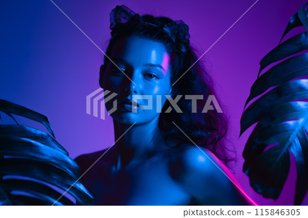 Woman in Neon Blue and Purple Lighting Surrounded by Tropical Leaves 115846305