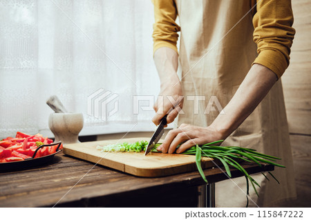 Unrecognizable man chopping spring onion with kitchen knife in the kitchen Unrecognizable man chopping spring onion with kitchen knife in the kitchen 115847222