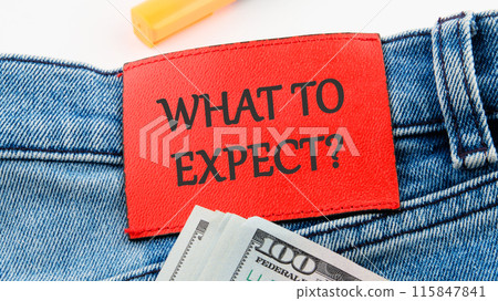 Business concept. WHAT TO EXPECT text on the red leather label of jeans on a white background in a composition with American dollars Business concept. WHAT TO EXPECT text on the red leather label of jeans on a white background in a composition with American dollars 115847841