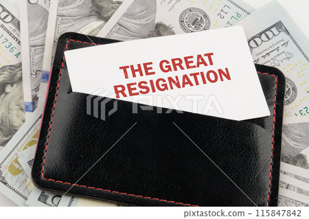 Text THE GREAT RESIGNATION on a business card in a black leather accessory against the background of American dollars 115847842