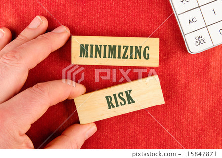 MINIMIZING RISK word written on wooden blocks with a hand, part of a calculator on a red background MINIMIZING RISK word written on wooden blocks with a hand, part of a calculator on a red background 115847871