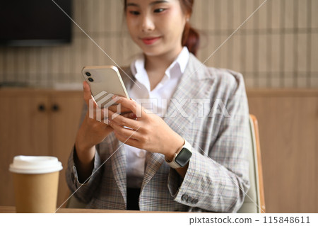 Select focus on hands. Smiling young businesswoman reading text on mobile phone sitting in modern office 115848611