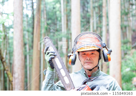一名森林工人拿著電鋸,直視前方,背景是一片維護良好的森林 一名森林工人拿著電鋸,直視前方,背景是一片維護良好的森林 115849163