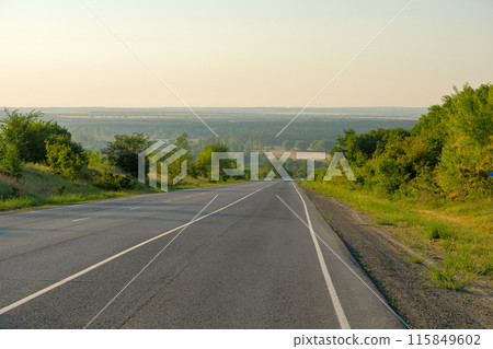 An empty asphalt road stretches to the horizon in the dawn haze. An empty asphalt road stretches to the horizon in the dawn haze. 115849602