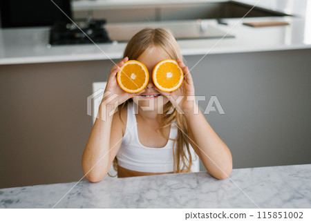 Child holding orange slice in front of her eyes at the kitchen table Child holding orange slice in front of her eyes at the kitchen table 115851002