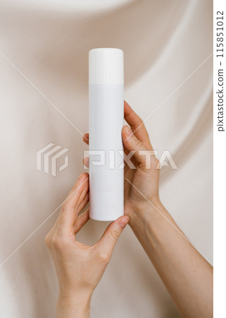 Woman's hands holds a bottle in her hands against a background of soft organza fabric 115851012