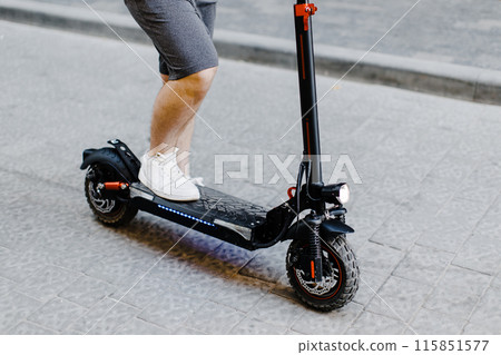 Cropped image of man in shorts and sneakers stepping on electric scooter while standing on city street Cropped image of man in shorts and sneakers stepping on electric scooter while standing on city street 115851577
