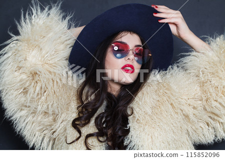 Charming young adult woman fashion model with bright make-up and long wavy hair wearing blue hat Charming young adult woman fashion model with bright make-up and long wavy hair wearing blue hat 115852096
