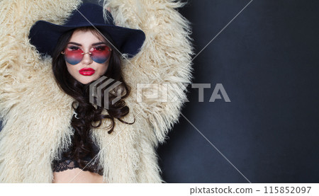 Glamorous young adult woman fashion model with bright make-up and long wavy hair wearing blue hat Glamorous young adult woman fashion model with bright make-up and long wavy hair wearing blue hat 115852097