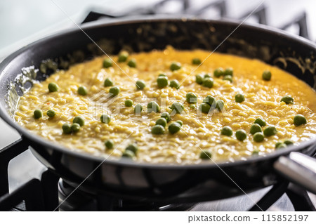 Saffron risotto with peas cooked in a pan on a gas stove 115852197
