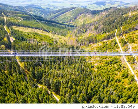 Aerial view of Sky Bridge 721, the worlds longest suspension footbridge, stretching across a forested valley in Czechia. People can be seen walking across the bridge, enjoying the scenic views. 115853549