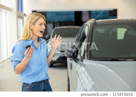 Pretty long-haired blonde woman near a new car looking enjoyed and excited 115853658