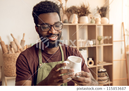 Dark-skinned sculptor working in his workshop and looking involved Dark-skinned sculptor working in his workshop and looking involved 115853687