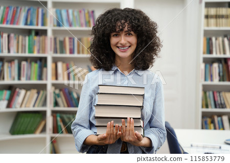 Smiling female librarian with a pile of books in hands 115853779