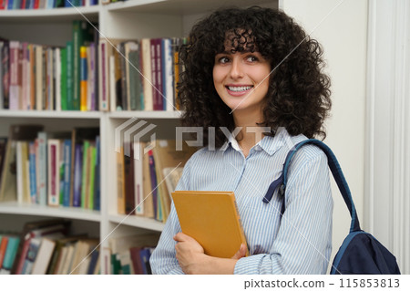 Cute woman in the library smiling nicely and looking contented Cute woman in the library smiling nicely and looking contented 115853813