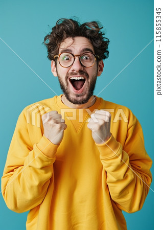 Excited Young Man in Yellow Sweater Expressing Joy with Fists Raised 115855345