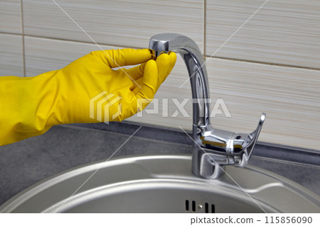 A worker in yellow rubber gloves unscrews a kitchen faucet aerator. Home repair 115856090