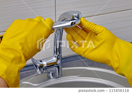 Kitchen faucet repair. A worker in yellow rubber gloves uses an adjustable wrench to unscrew the aerator 115856118