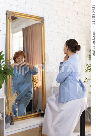 Young attractive woman looks at mirror and see elderly woman, mature herself from future, smiling joyfully to her. Young attractive woman looks at mirror and see elderly woman, mature herself from future, smiling joyfully to her. 115859435