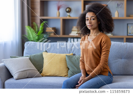 Confident young woman sitting on couch in modern living room with stylish decor. Relaxed and calm atmosphere. Natural light creating cozy ambiance. Confident young woman sitting on couch in modern living room with stylish decor. Relaxed and calm atmosphere. Natural light creating cozy ambiance. 115859873
